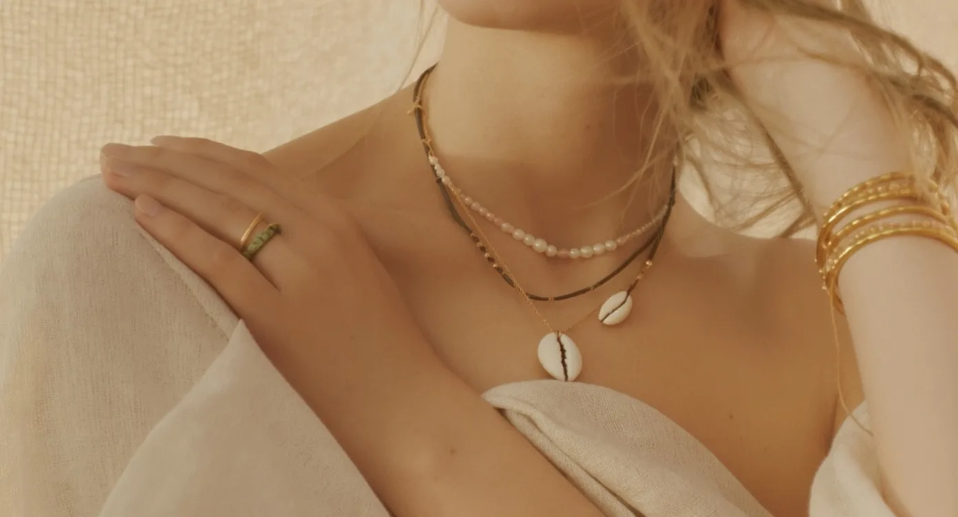Layered shell necklaces of different lengths worn together with a stack of thin gold bracelets on the wrist